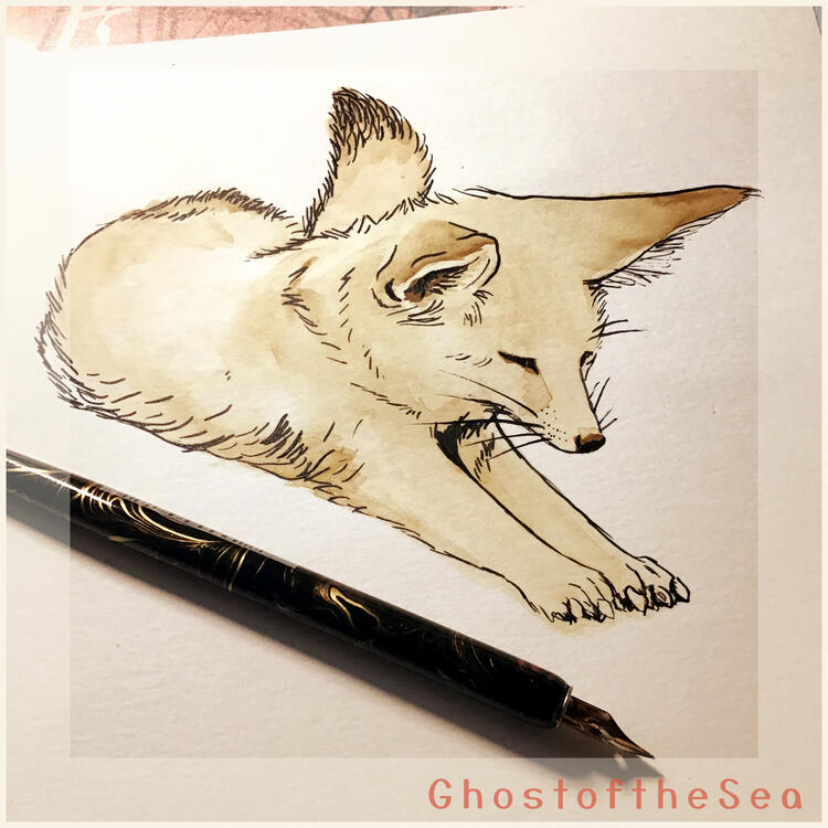 Photo of a simple A5 watercolour painting of a fennec fox laying down and looking content. Only a single sepia-toned colour is used, along with blank ink for outlines. There is a black and gold dip pen lay across the image.
